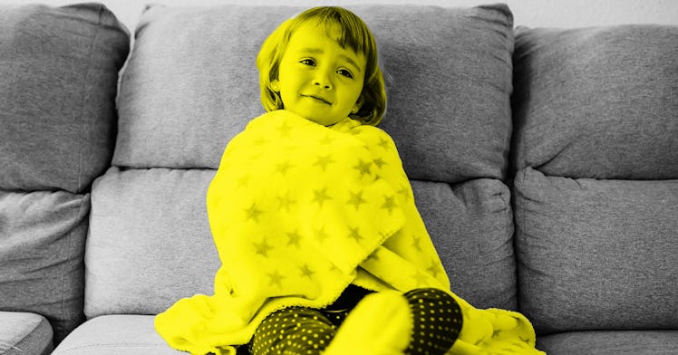 A toddler with flu symptoms sits on a couch wrapped in a blanket. yellow color filter