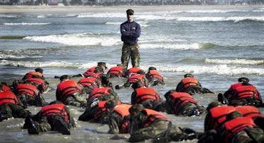Navy Seals on the ground at a beach during hell week, with a drill sergeant standing in front of the...