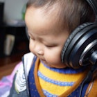 A baby in blue and orange clothes listening to an audiobook via large black headphones on its head