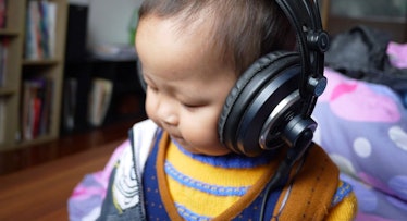 A baby in blue and orange clothes listening to an audiobook via large black headphones on its head