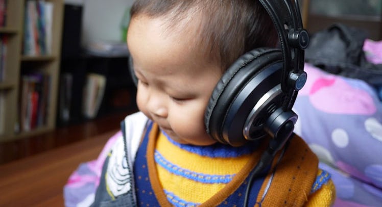 A baby in blue and orange clothes listening to an audiobook through large black headphones on its he...
