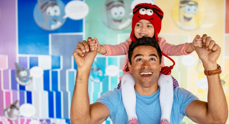 A little girl sitting on her father's shoulders, both of them smiling at a toy factory tour