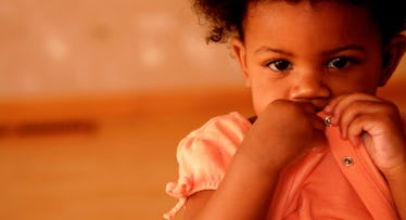 shy toddler wearing a pink dress and covering mouth
