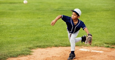 A kid playing baseball as a pitcher in the little league is throwing a pitch while wearing his teams...