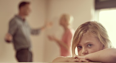 A child sulks while her parents fight in the background.