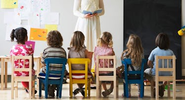 Six kids sitting on chairs while their teacher reads to them in Pre-K