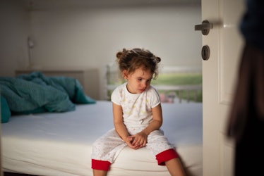 A kid sitting on a bed looking sad.