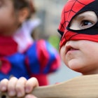 Little boy dressed up as Spiderman, holding a wooden bat.
