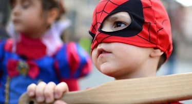 A little boy dressed up as Spiderman, holding a wooden bat.
