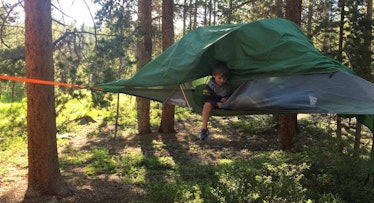 A toddler getting out of a tree tent in the middle of the woods