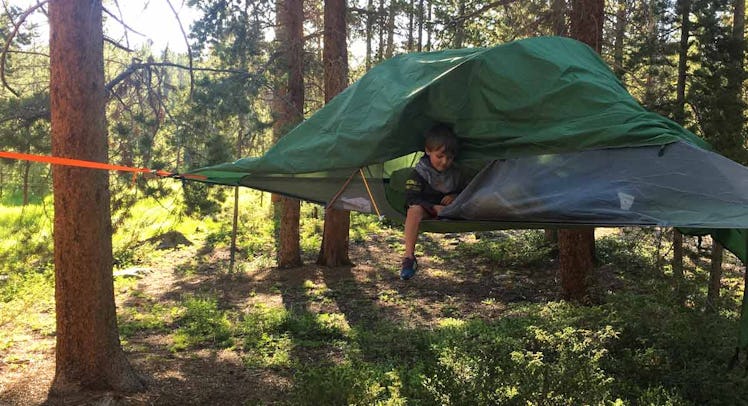 A toddler getting out of a tree tent in the middle of the woods