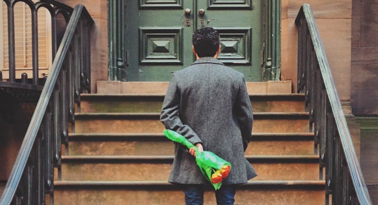 man standing on stoop holding flowers