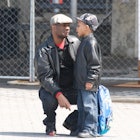 A father squatting next to his son on the street telling him something during day time