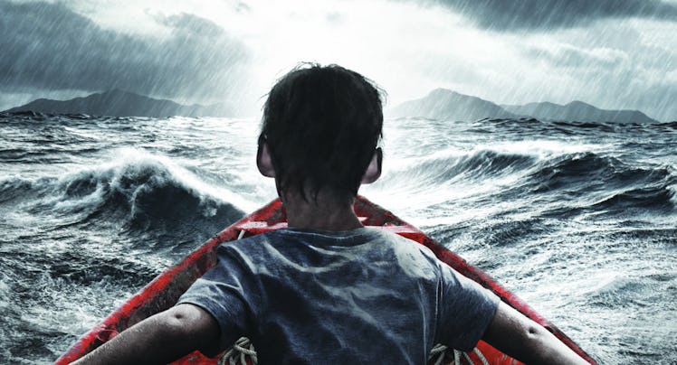 A refugee boy sitting in a red boat in the middle of a thunderstorm over the sea