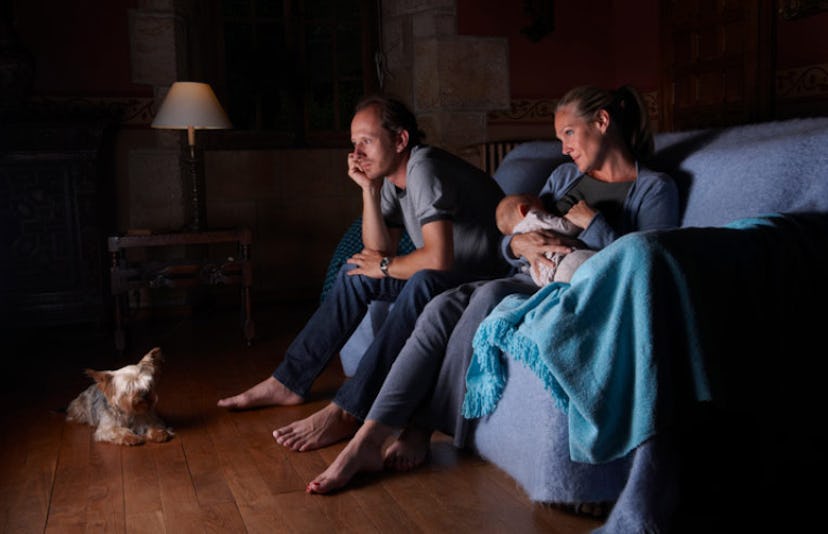 Couple watching television together while woman is holding their baby