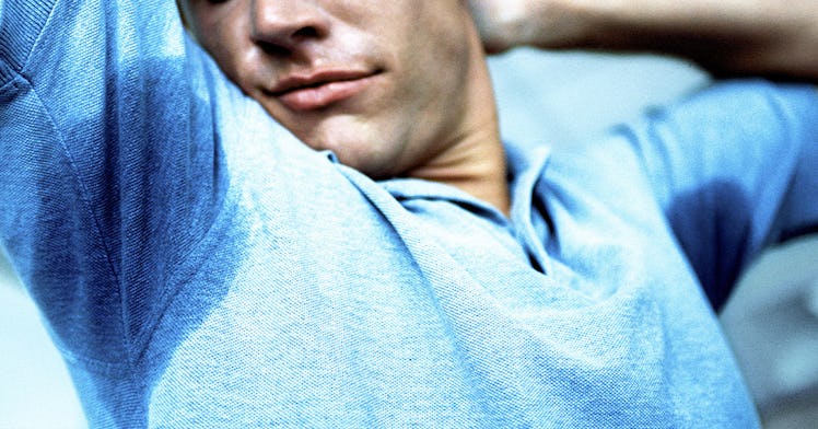 A man stretching with visible sweat stains on his armpits
