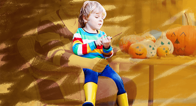 A dad who is barely visible holding his son who is wearing brightly striped clothing next to Hallowe...