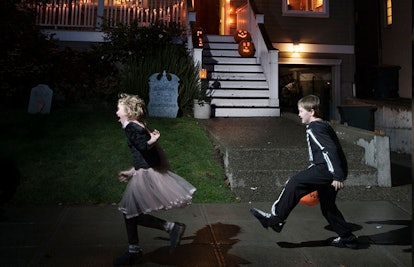 Two children in Halloween costumes running down the street while trick or treating next to a decorat...