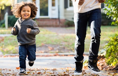 A young little boy running down a street with his father and laughing