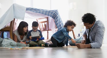 Kids playing with their parents in a fort made of kitchen chairs and a table cloth 