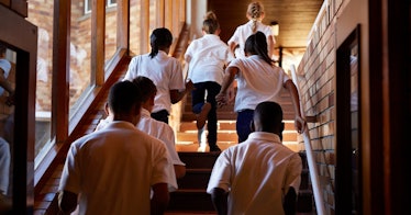 high-contrast color photo of public or private school kids running up the school stairs