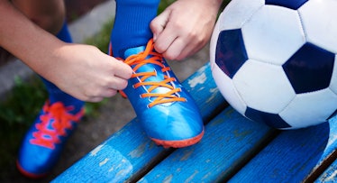 A young pair of hands ties a shoe next to a soccer ball