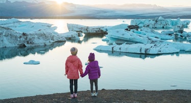 Two children stand holding hands and look at glaciers melted by climate change