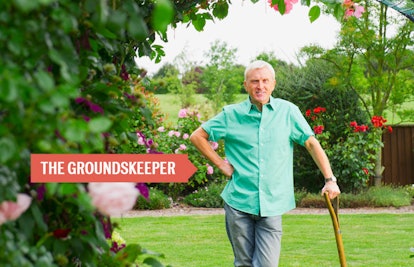 An older man standing in his garden putting his weight on his gardening tool with a sign that says t...