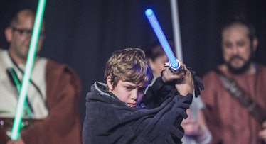 A young boy dressed up as Anakin waving with his lightsaber