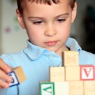 child in blue polo shirt plays with blocks