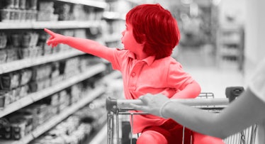 A toddler boy sitting in a shopping cart and looking at grocery products