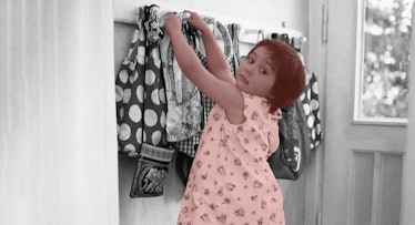 A little girl hanging her jacket on a cloth rack on a wall as it is a routine that helps the family ...