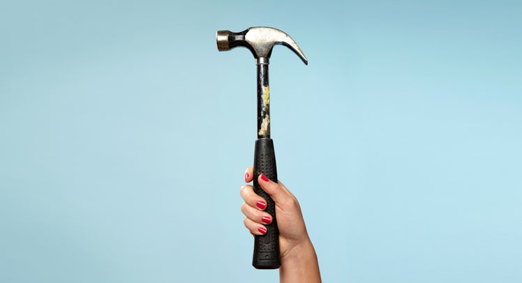 A female hand with red nails holding a hammer