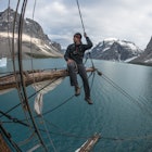 Mike Libecki on a fighting top of a ship with the sea and mountains in the background