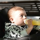 A baby in a stroller outside drinking a toddler drink from a bottle that could be harmful