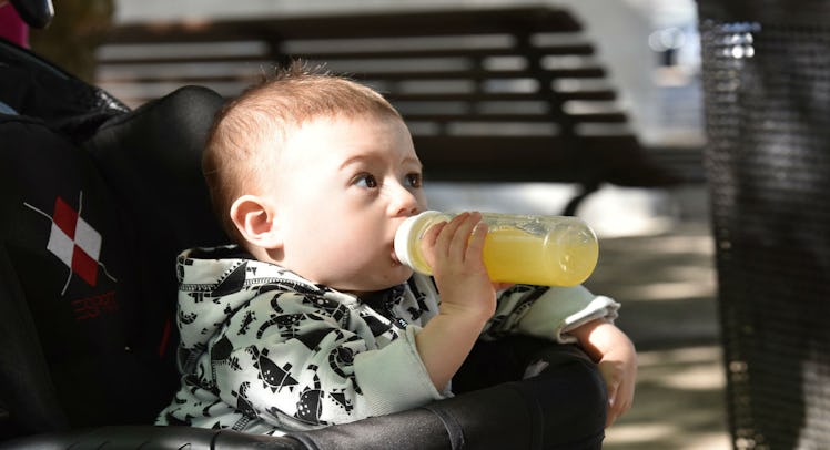 A baby in a stroller outside drinking a toddler drink from a bottle 