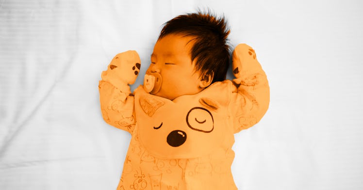newborn baby sleeping in sleep sack with arms above head and pacifier in mouth