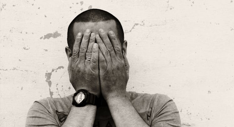 A middle-aged man covering his face with his hands in black and white