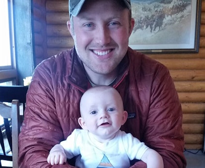 A man in a red puffy jacket and a green baseball cap holding his baby in his lap at a restaurant