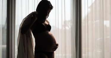 A half dressed pregnant women holds their stomach.