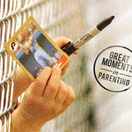 A young boy giving a baseball player card and a black marker for signing through a fence