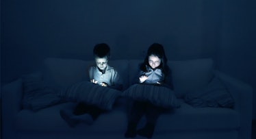 Two kids using their phones before bed in the dark.