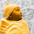 A 1-month-old baby is swaddled and laid to sleep on a bed