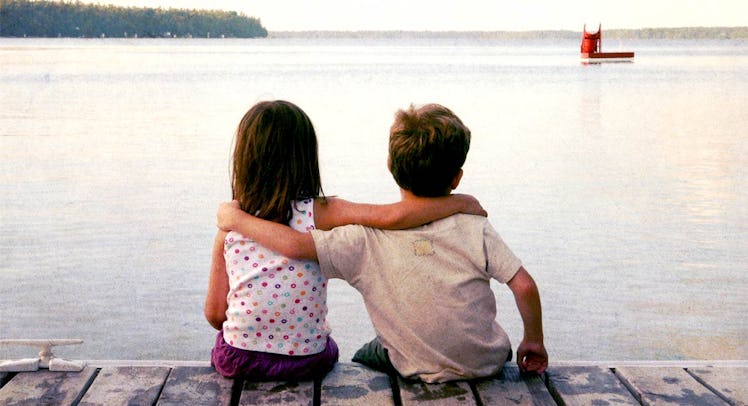 A little boy sitting next to his girl best friend and hugging her as they look at the sea