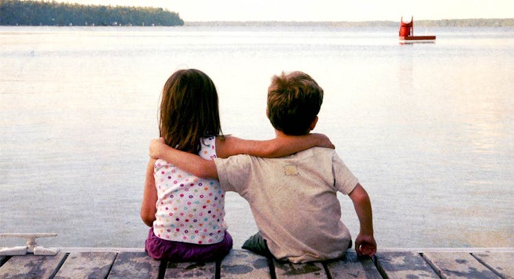 A little boy sitting next to his girl best friend and hugging her as they look at the sea 