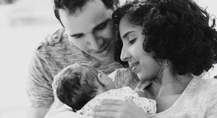 greyscale edit of mother holding newborn baby and father looking over her shoulder adoringly