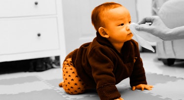 baby crawling on the ground as a parent uses a napkin to wipe snot off their nose