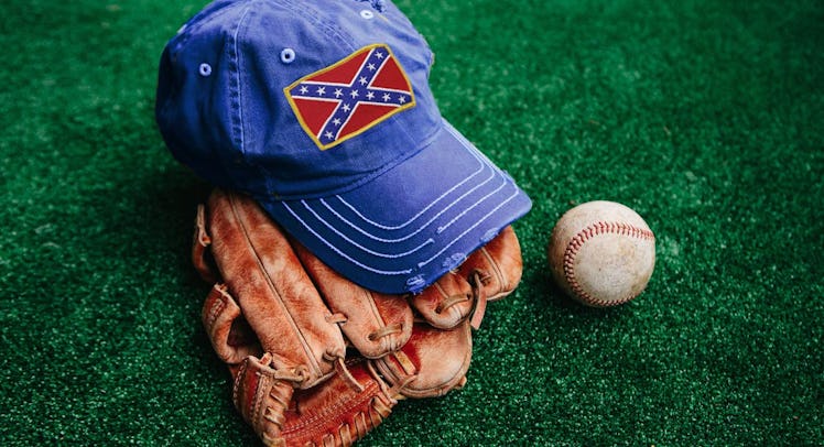 A blue cap on a brown baseball glove and a ball next to it placed on the grass