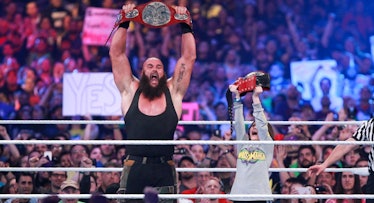 Braun Strowman of WWE and a child in the WWE ring holding trophy belts in the air with the audience ...