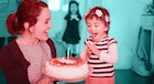 在一个孩子的生日派对上，一个戴着花冠的两岁孩子兴奋地吹灭了蛋糕上的蜡烛